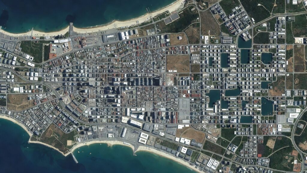 Vista satelital cenital de una ciudad costera con una franja de terreno artificial cuyas geometrías no encajan con el resto del mapa